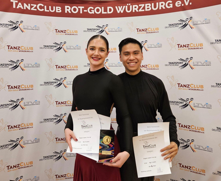 Tanzpaar mit Urkunden und Pokal vor TanzClub Rot-Gold Würzburg e.V. Banner