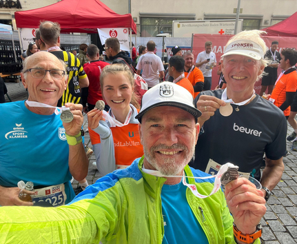 Selfie von vier Läufern die Medaillen nach 10 km zeigen