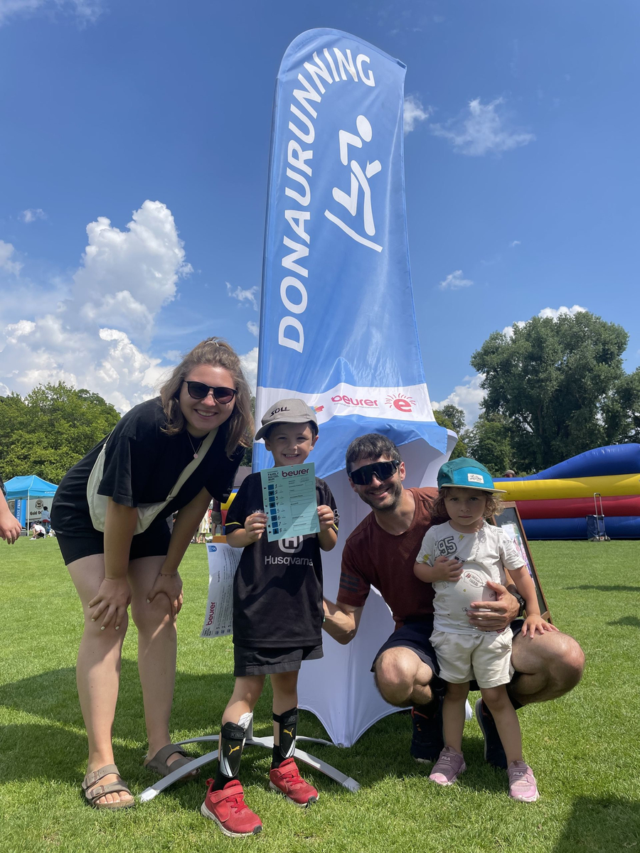 DONAURUNNING Family Rätsel Run powered by Beurer - SSV Ulm 1846 e.V. Schwörsporttag 2024 Familie mit zwei Kindern vor DONAURUNNING Fahne, Kind hält beurer Rätselplan