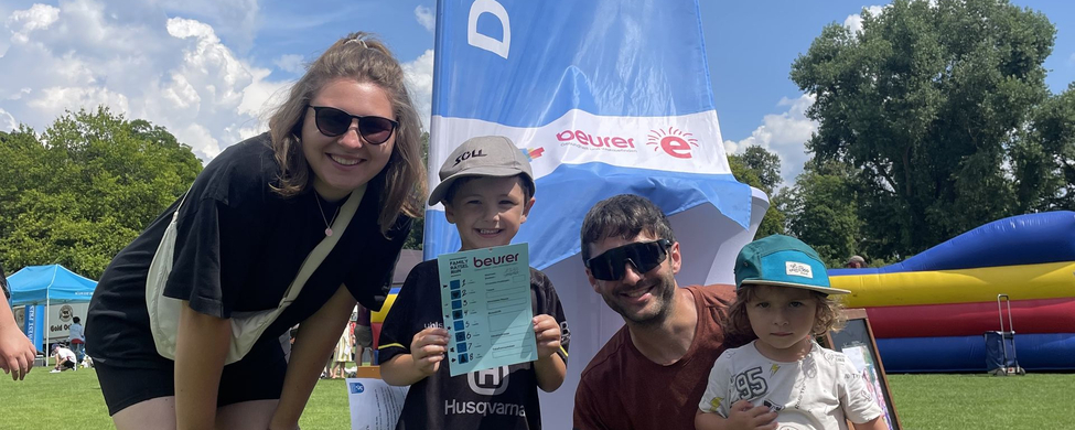 DONAURUNNING Family Rätsel Run powered by Beurer - SSV Ulm 1846 e.V. Schwörsporttag 2024 Familie mit zwei Kindern vor DONAURUNNING Fahne, Kind hält beurer Rätselplan