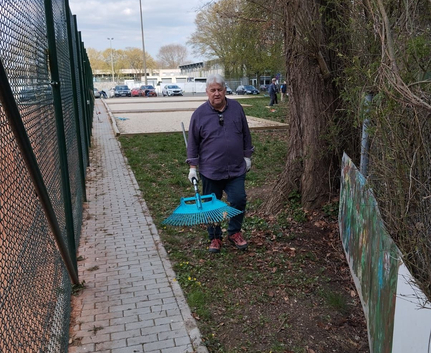 Teilnehmer der Putzete 2025 mit blauem Rechen und Handschuhen neben Gehweg