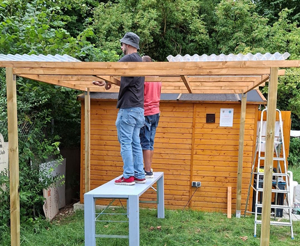 Zwei Personen montieren Dachplatten an Erweiterung der Vereinshütte