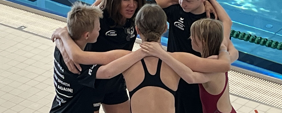 Schwimmtrainerin und vier junge Athletinnen und Athleten im Kreis am Beckenrand