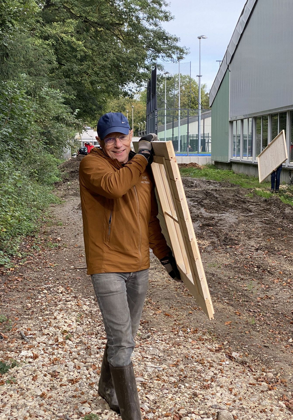Mann mit blauer Kappe trägt Holzrahmen entlang Schotterweg