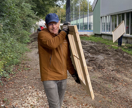 Mann mit blauer Kappe trägt Holzrahmen entlang Schotterweg