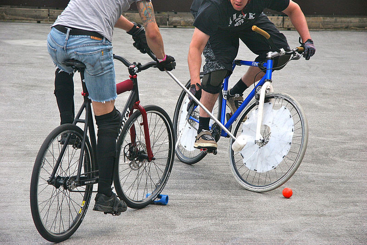 Zwei Bikepolo-Spieler auf Fahrrädern mit Schlägern und orangefarbenem Ball