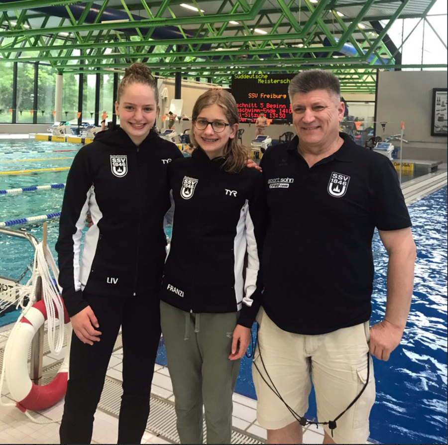Trainer mit zwei jungen Schwimmerinnen am Beckenrand