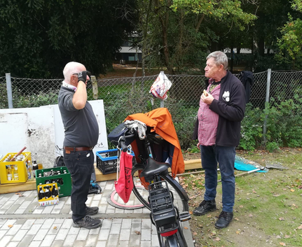 Zwei Männer stehen neben Fahrrad und Getränkekisten, einer isst