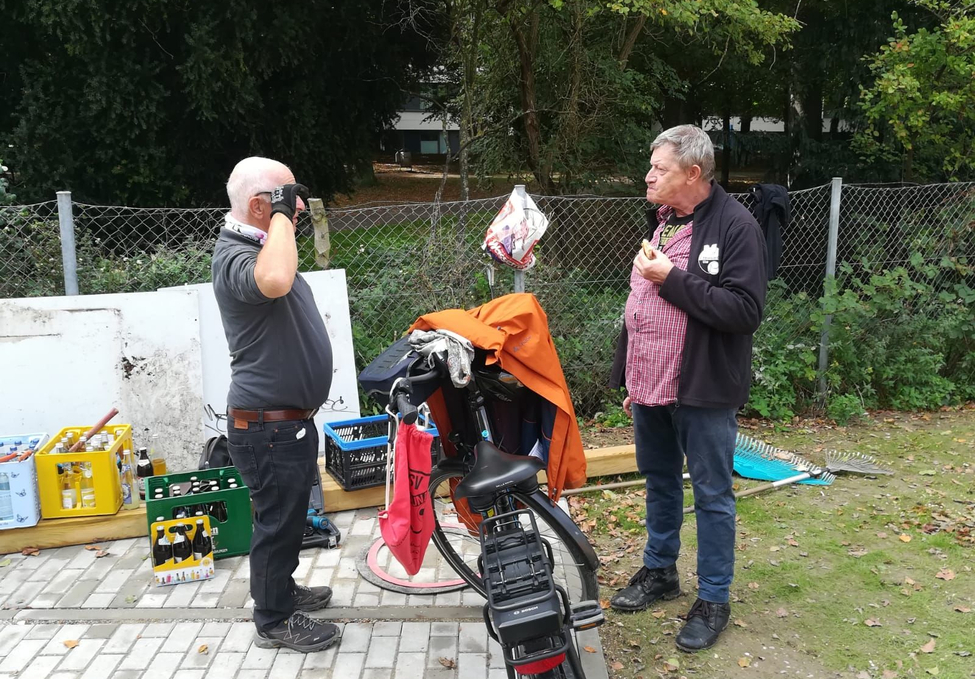 Zwei Männer stehen neben Fahrrad und Getränkekisten, einer isst