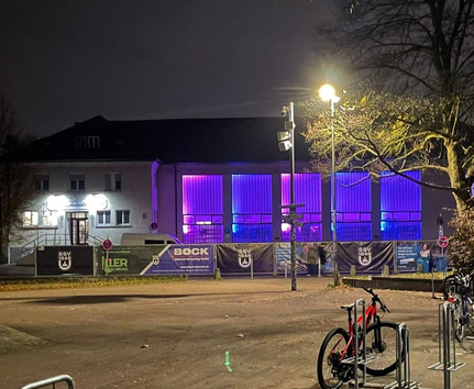 Jahnhalle außen bei Nacht mit lila beleuchteten Fenstern und Fahrrädern im Vordergrund