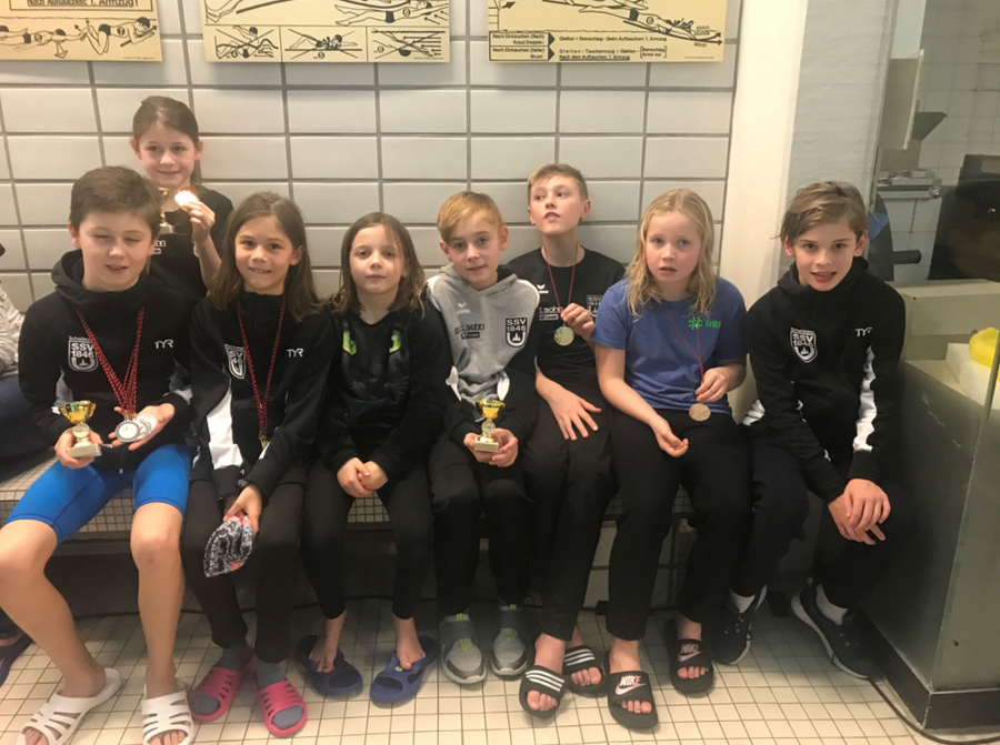 Junge Schwimmer sitzen mit Medaillen und Pokalen