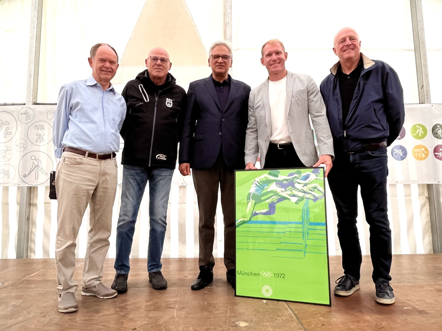 Fünf Personen auf einer Bühne mit gerahmtem München 1972 Plakat