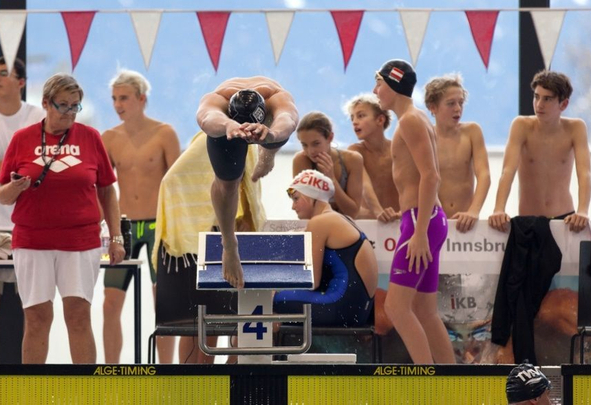 Schwimmer springt vom Startblock Nummer 4 andere Schwimmer im Hintergrund