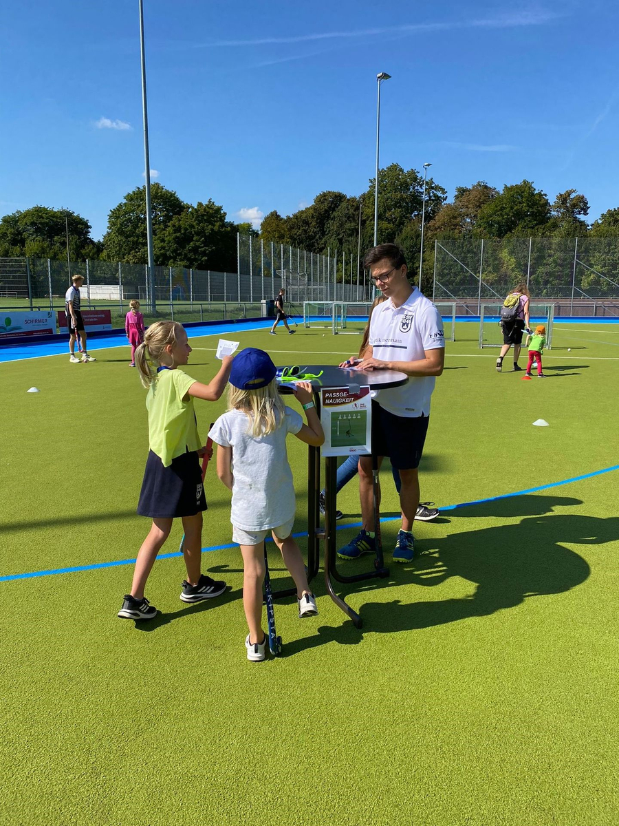 Trainer an Stehtisch mit zwei Kindern und Hockeyschlägern auf Hockeyplatz