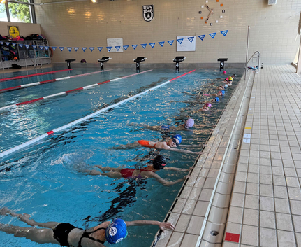 Mehrere Nachwuchsschwimmer in Schwimmkappen am Beckenrand