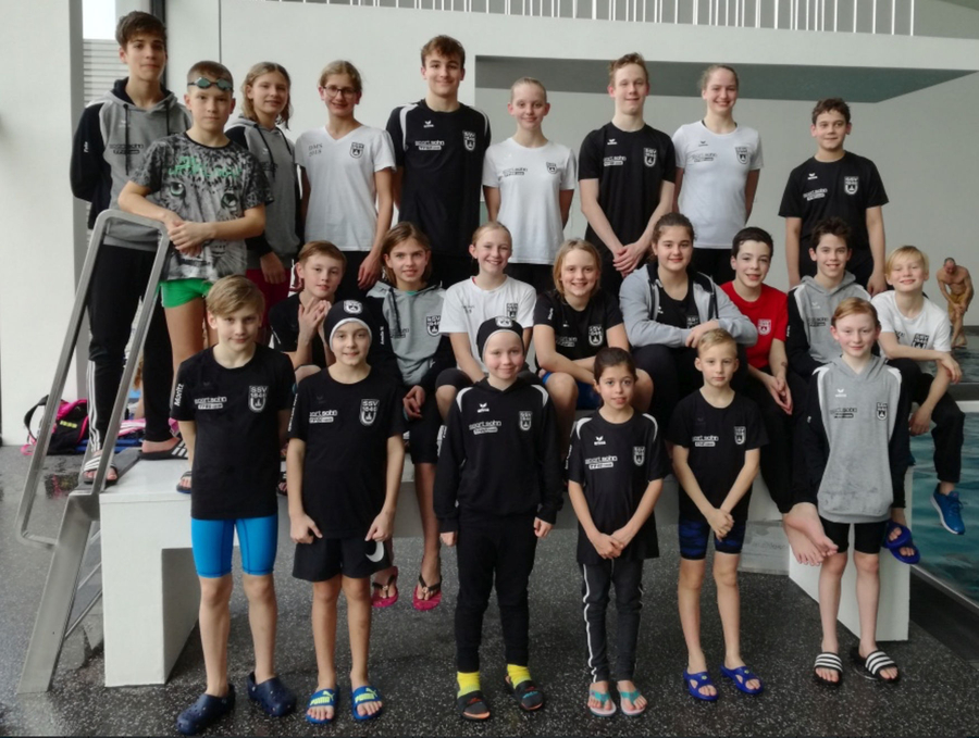 Jugendliches Schwimmteam in Vereinskleidung vor Hallenbad