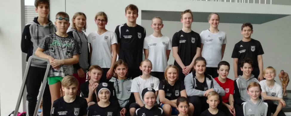 Jugendliches Schwimmteam in Vereinskleidung vor Hallenbad