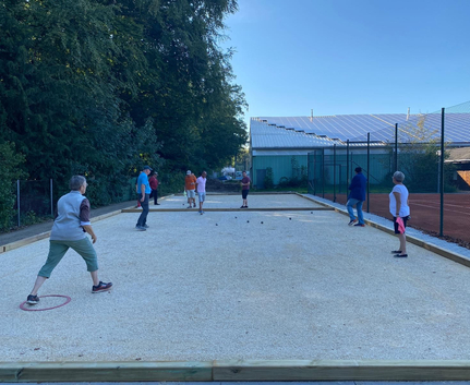 Gruppe spielt Boule auf rechteckigem Kiesplatz neben Tennisanlage