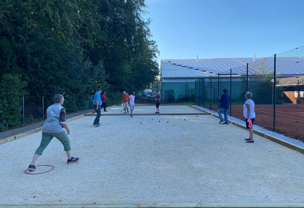 Gruppe spielt Boule auf rechteckigem Kiesplatz neben Tennisanlage