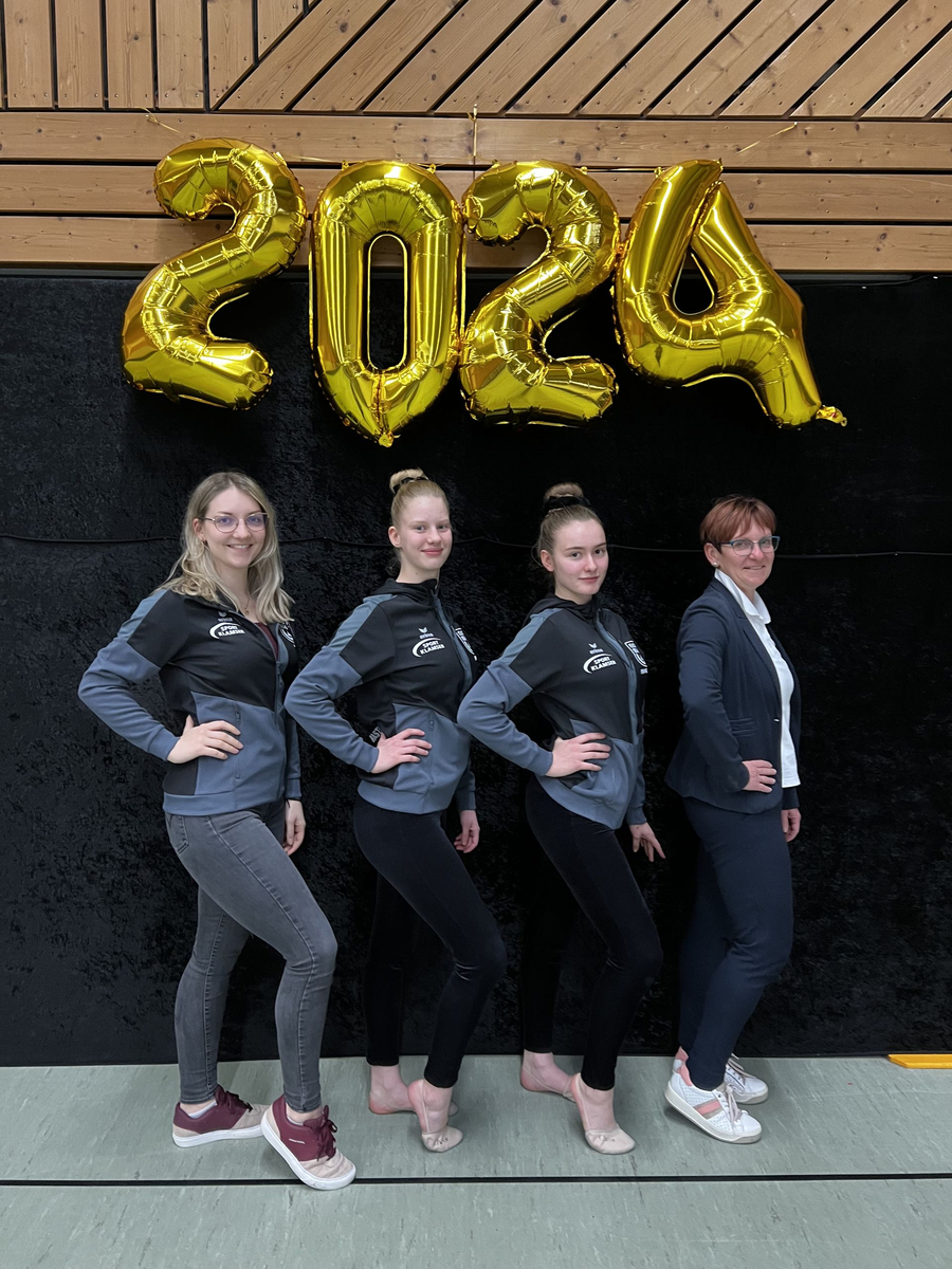Vier nebeneinander stehende Personen vor goldenen Ballons mit 2024