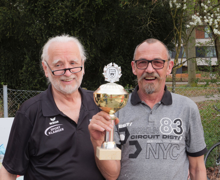 Two older men smiling and holding a gold trophy