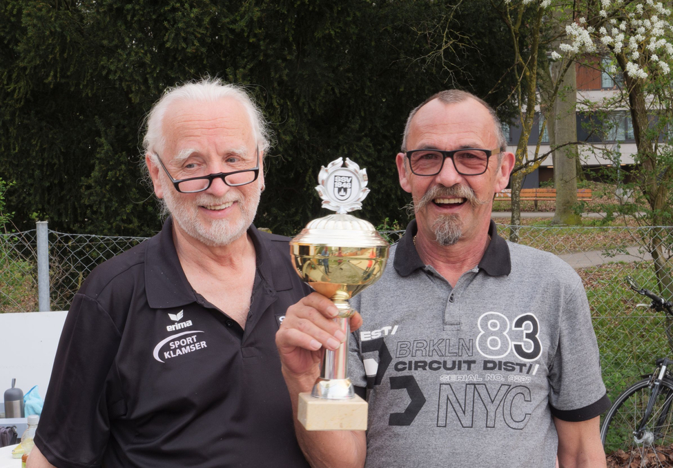 Two older men smiling and holding a gold trophy