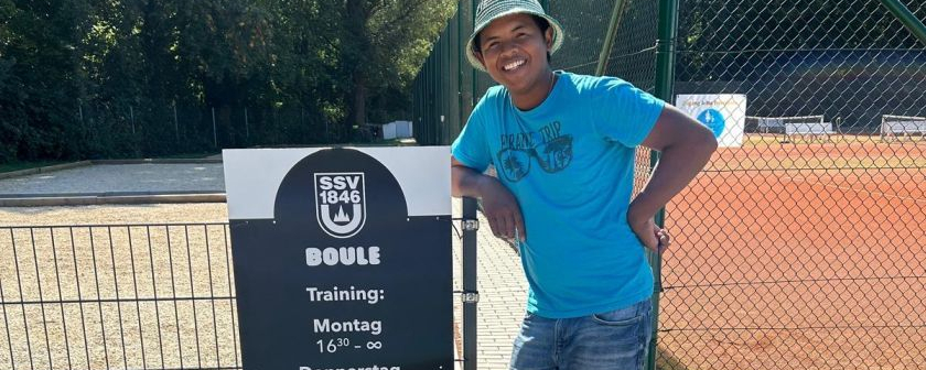Person lehnt an Tafel mit Text BOULE Training Montag Donnerstag