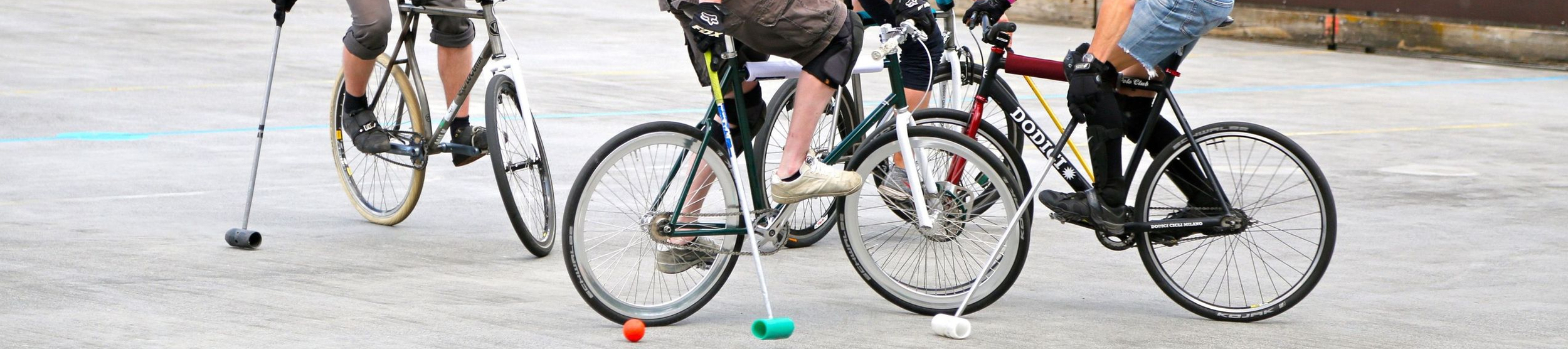 Vier Spieler auf Fahrrädern mit Schlägern und Helmen um einen orangenen Ball