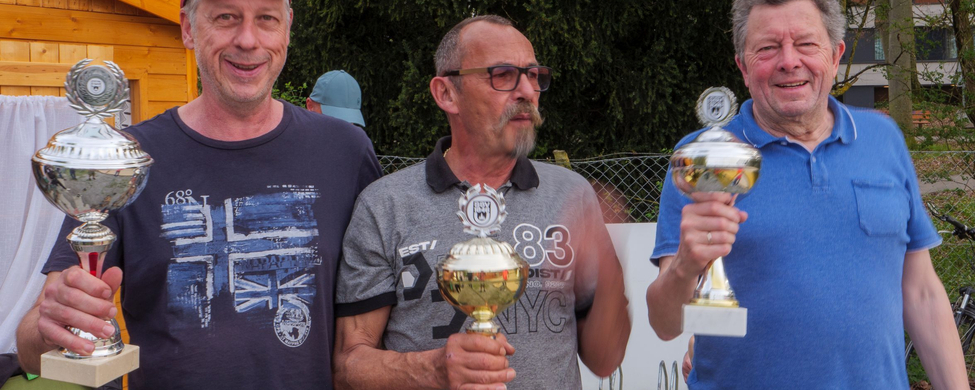 Drei Männer im Freien halten Pokale, T-Shirt mit 83 NYC sichtbar