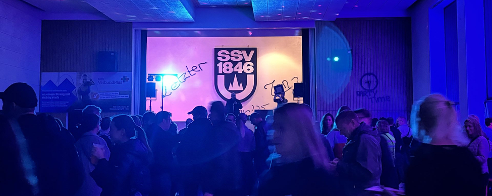 Menschen in blauviolett beleuchteter Sporthalle vor SSV 1846 Wandlogo