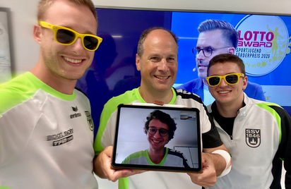 Drei Männer in Sportshirts, zwei mit gelben Sonnenbrillen, Tablet mit Videoanruf LOTTO