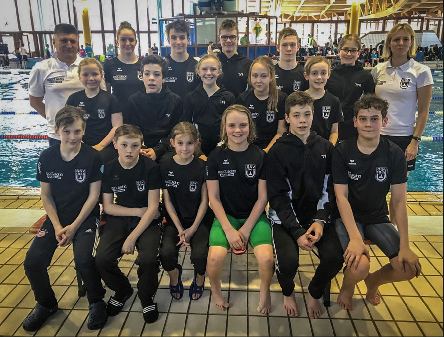 Jugendliche Schwimmer und Trainer als Team neben Wettkampfbecken
