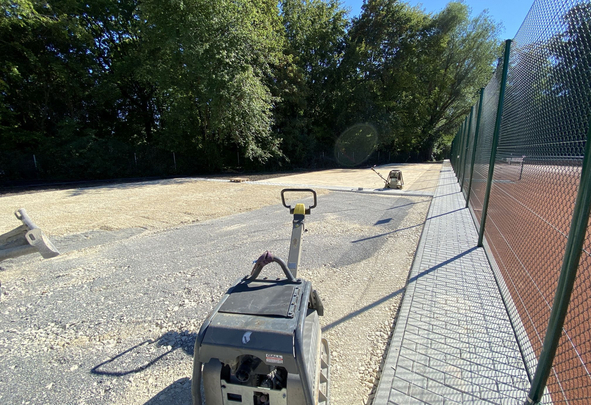Baustelle mit Rüttelplatten auf geschottertem Untergrund neben Tenniszaun