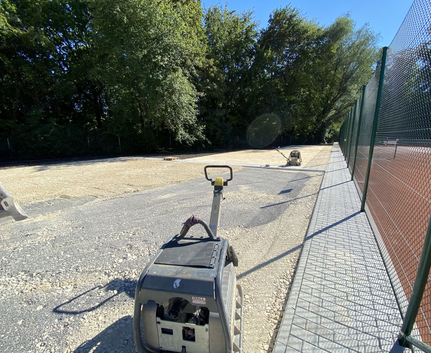Baustelle mit Rüttelplatten auf geschottertem Untergrund neben Tenniszaun