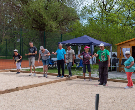 Mehrere Personen spielen Boule auf Kiesbahn neben blauem Pavillon