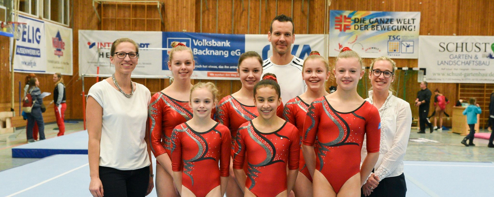 Turnerinnen in roten Turnanzügen in Sporthalle mit Trainern