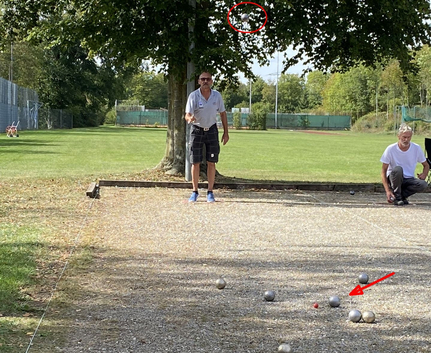 Zwei Männer spielen Boule auf Schotterbahn mit mehreren Metallkugeln und rotem Zielball
