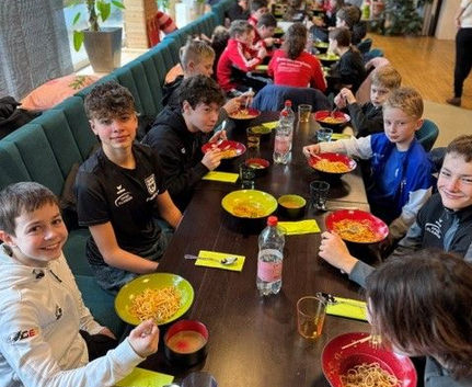Jugendliche Sportler sitzen an langem Tisch und essen Nudeln