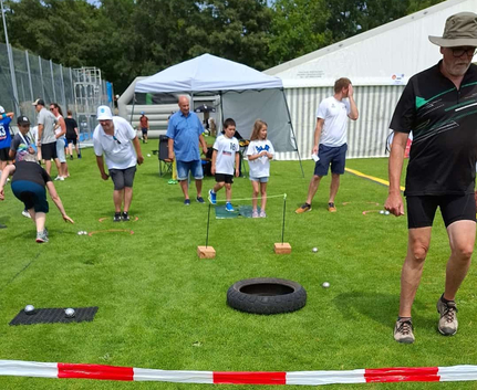 Mehrere Personen spielen Boule auf Rasen vor Pavillon