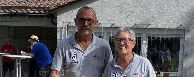Zwei Personen in grauen Poloshirts stehen auf Kies neben einem roten Ring