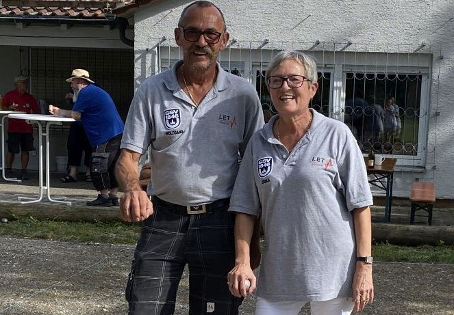 Zwei Personen in grauen Poloshirts stehen auf Kies neben einem roten Ring