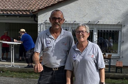 Zwei Personen in grauen Poloshirts stehen auf Kies neben einem roten Ring
