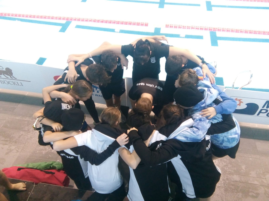Jugendliche Schwimmer in Gruppenumarmung am Beckenrand