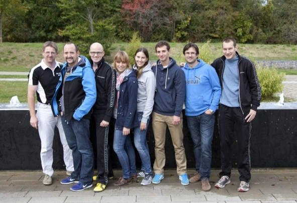 Neun Erwachsene in Freizeitkleidung nebeneinander vor Springbrunnen