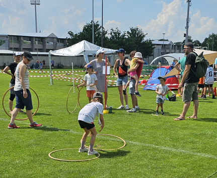 Kinder und Erwachsene auf Sportwiese mit Hula-Hoops und Zelt