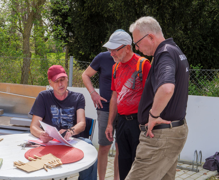Vier Männer prüfen Unterlagen an einem runden Gartentisch