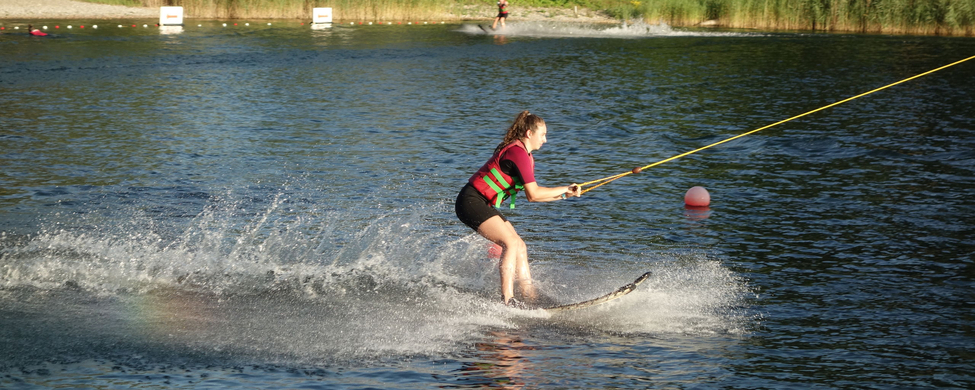 Jugendliche mit Schwimmweste beim Wasserski an einer Seilbahn am See