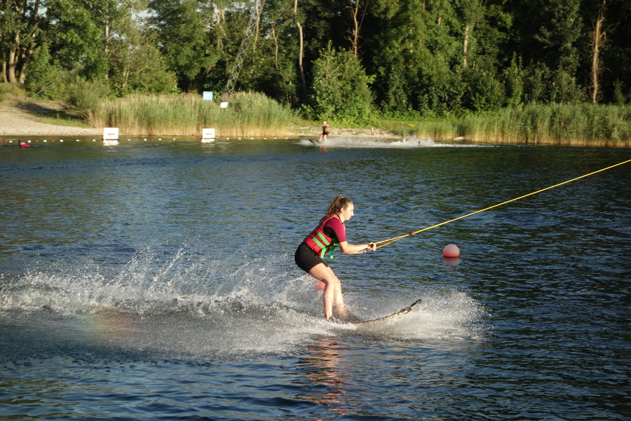 Jugendliche mit Schwimmweste beim Wasserski an einer Seilbahn am See