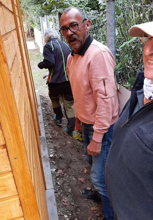 Mann mit Brille und rosa Pullover zwischen Holzwand und Zaun