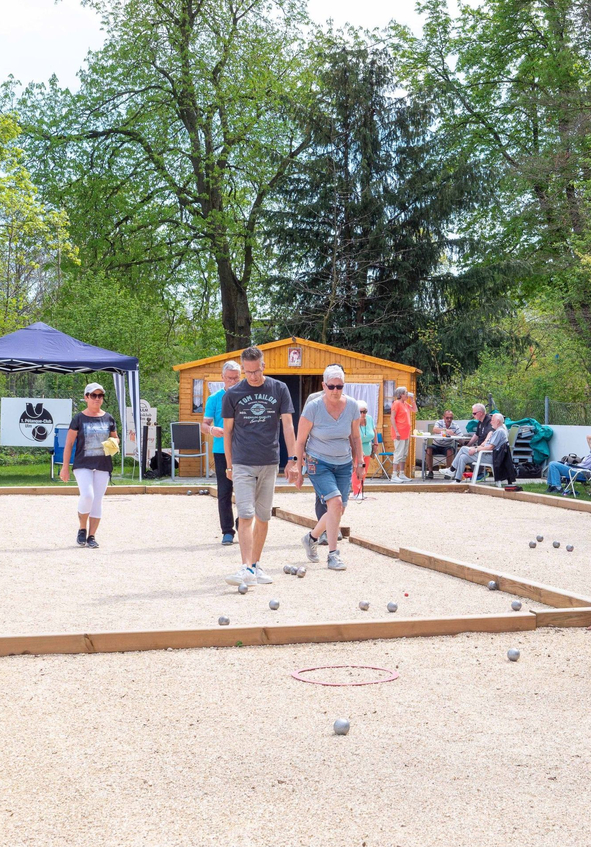 Gruppe Menschen spielt Petanque auf Sandbahnen mit Metallkugeln unter Bäumen